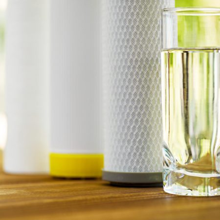 A glass of purified water and filter cartridges on wooden table on green natural background