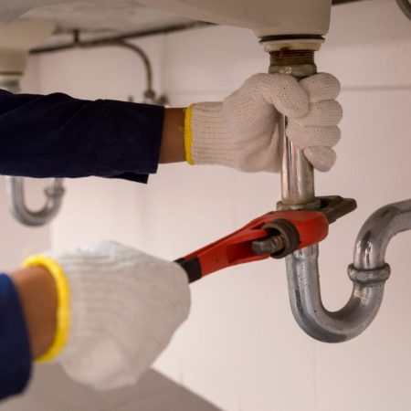 Plumber fixing white sink pipe with adjustable wrench.